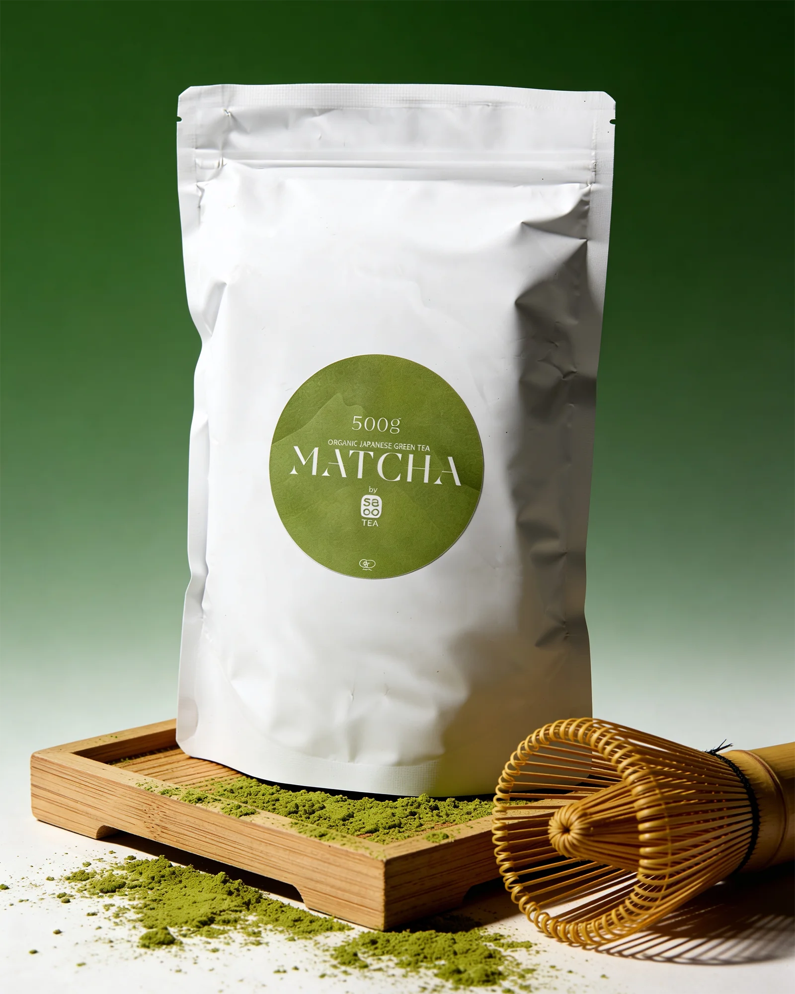 White package of matcha (500g) with a green label on a wooden tray with matcha powder and a whisk.