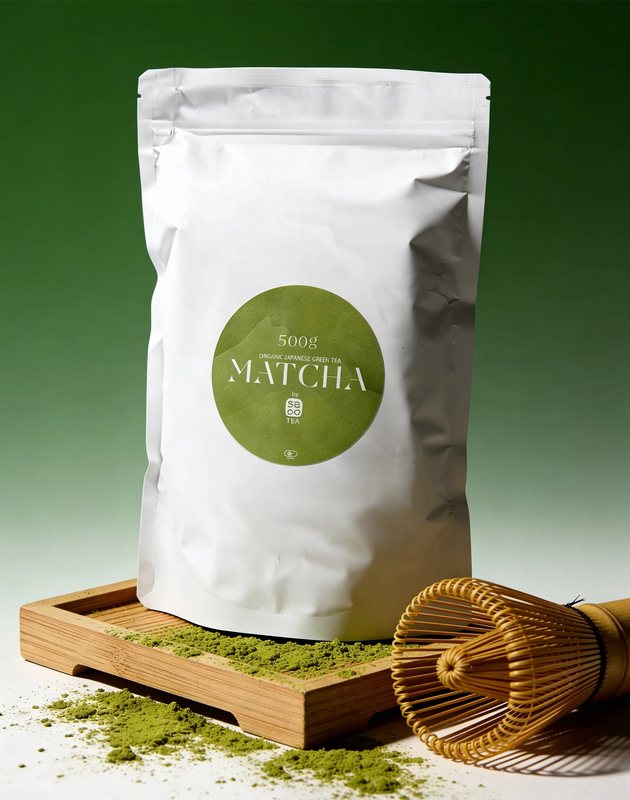 White package of matcha (500g) with a green label on a wooden tray with matcha powder and a whisk.