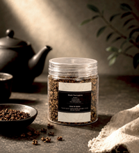 Jar of black tea leaves on a dark surface with a teapot and cloth in the background
