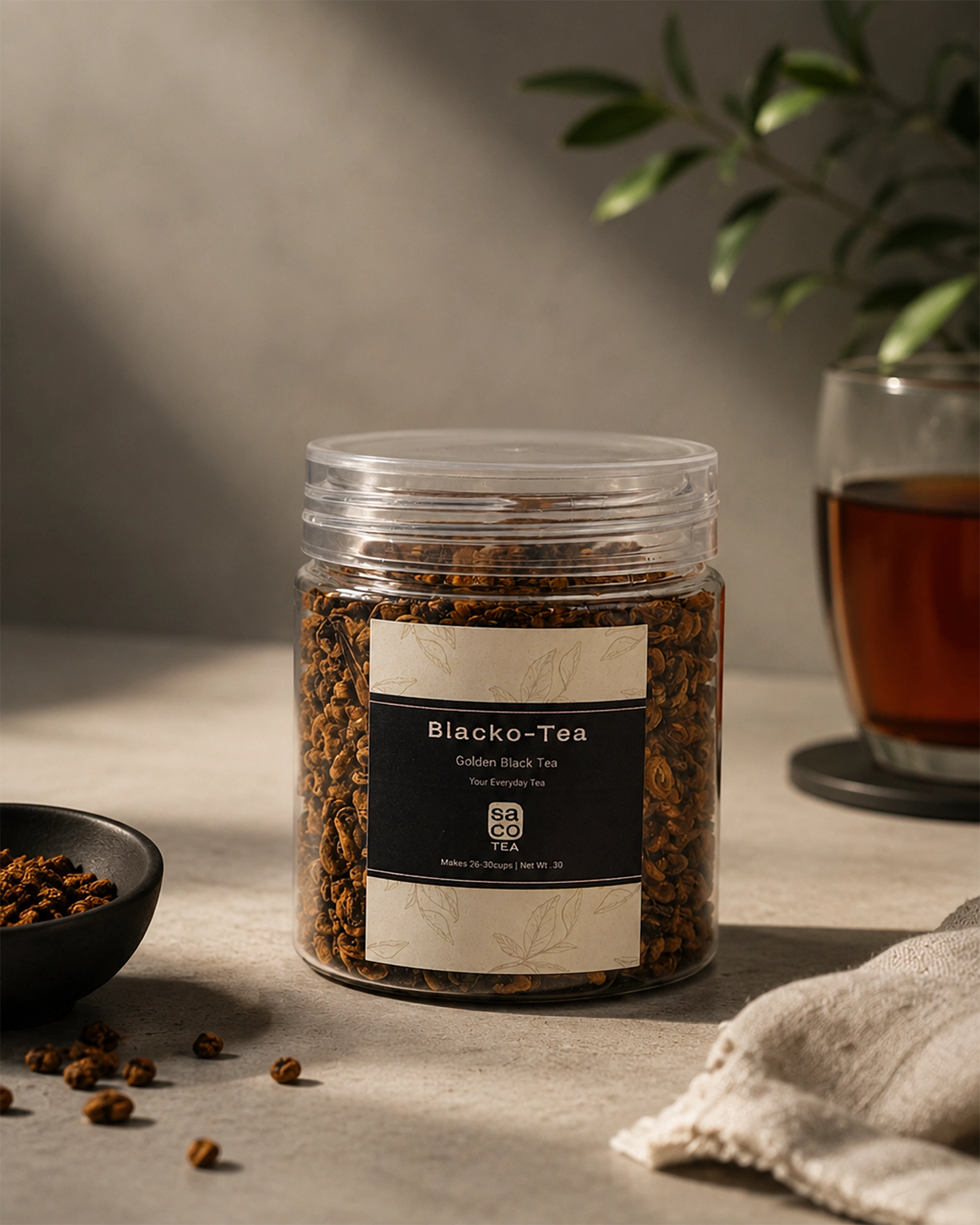 Jar of Blacko-Tea with a glass of tea in the background on a neutral surface.