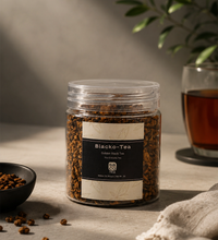 Jar of Blacko-Tea with a glass of tea in the background on a neutral surface.