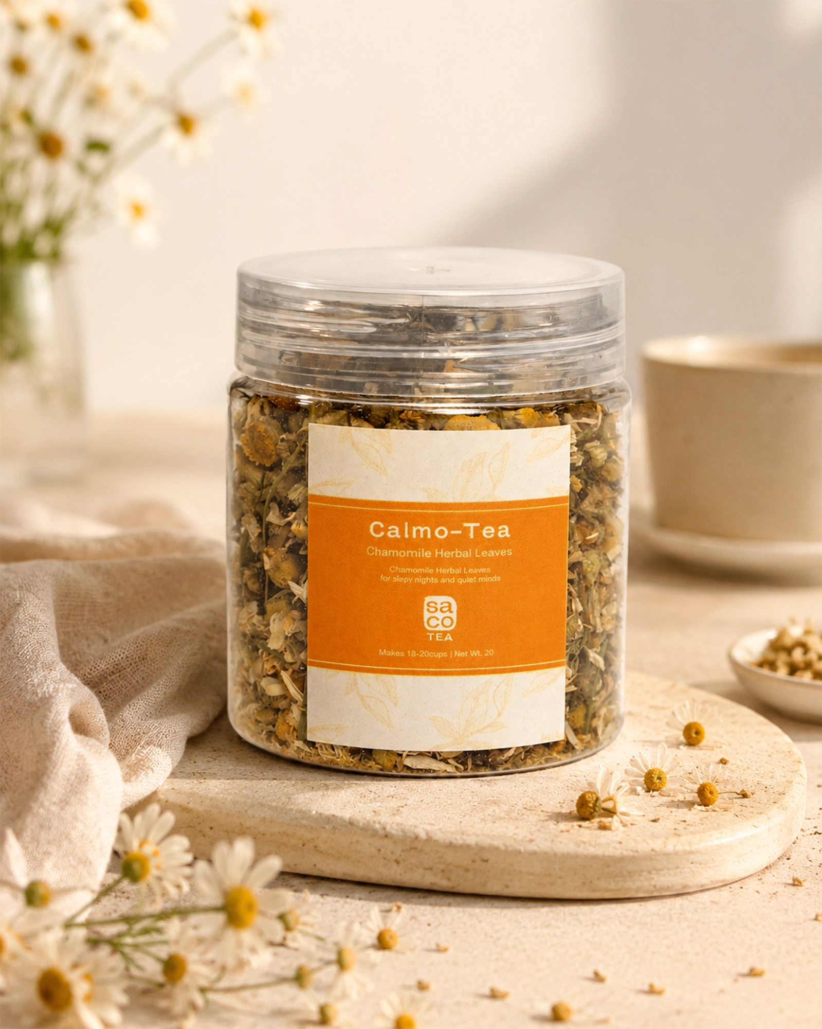Jar of Calmo-Tea with a label on a wooden coaster with flowers and a cup in the background.