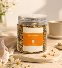 Jar of Calmo-Tea with a label on a wooden coaster with flowers and a cup in the background.