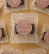 Brüt Bar chocolate mini packages with pink labels arranged on a beige background.
