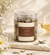 Jar of Silver Needle White Tea with loose tea leaves, white flowers, and a cup of tea on a soft neutral background