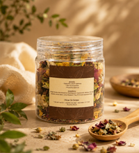 Saco Tea Signature herbal tea jar with dried flowers, loose herbs, and a wooden spoon on a warm beige surface.