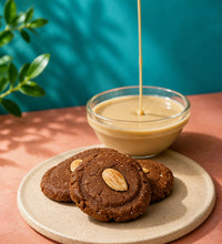 Chewy tahini cookies with almonds on a ceramic plate beside a bowl of creamy tahini sauce.