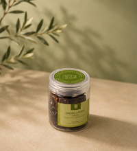 Saco Tea Green Heart Dates jar on a beige surface with soft olive branch shadows.