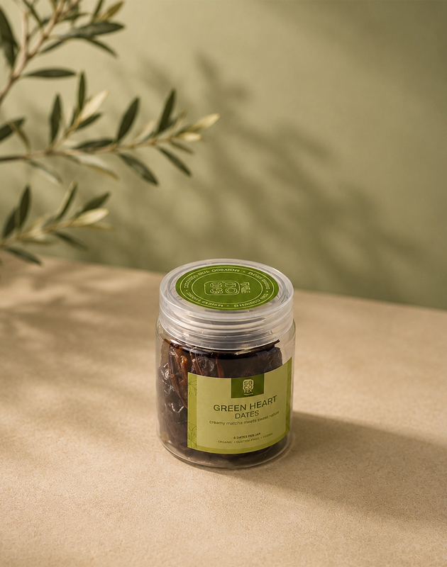 Saco Tea Green Heart Dates jar on a beige surface with soft olive branch shadows.