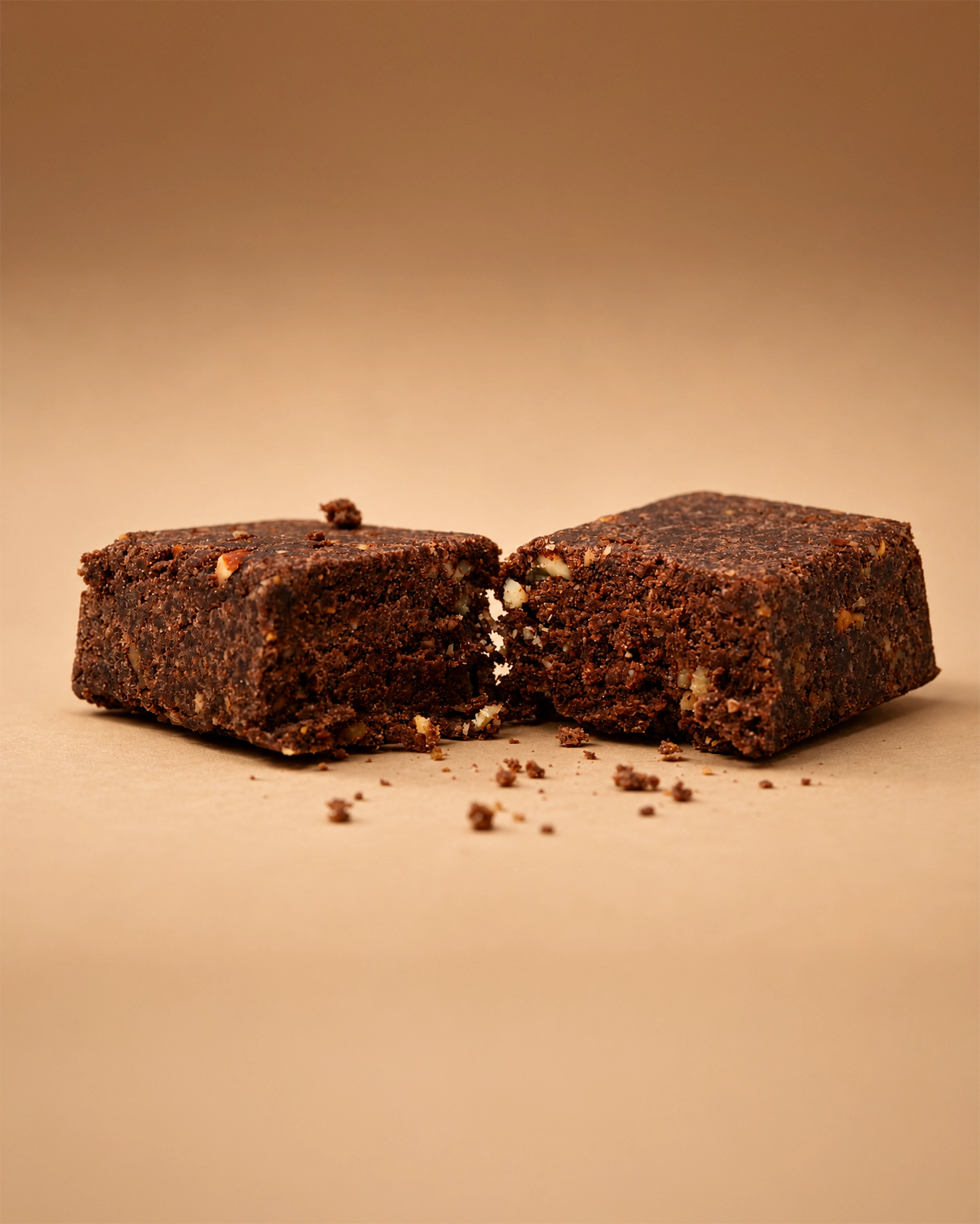 Two Brüt Minis chocolate bars broken open with crumbs on a beige background.