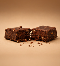 Two Brüt Minis chocolate bars broken open with crumbs on a beige background.