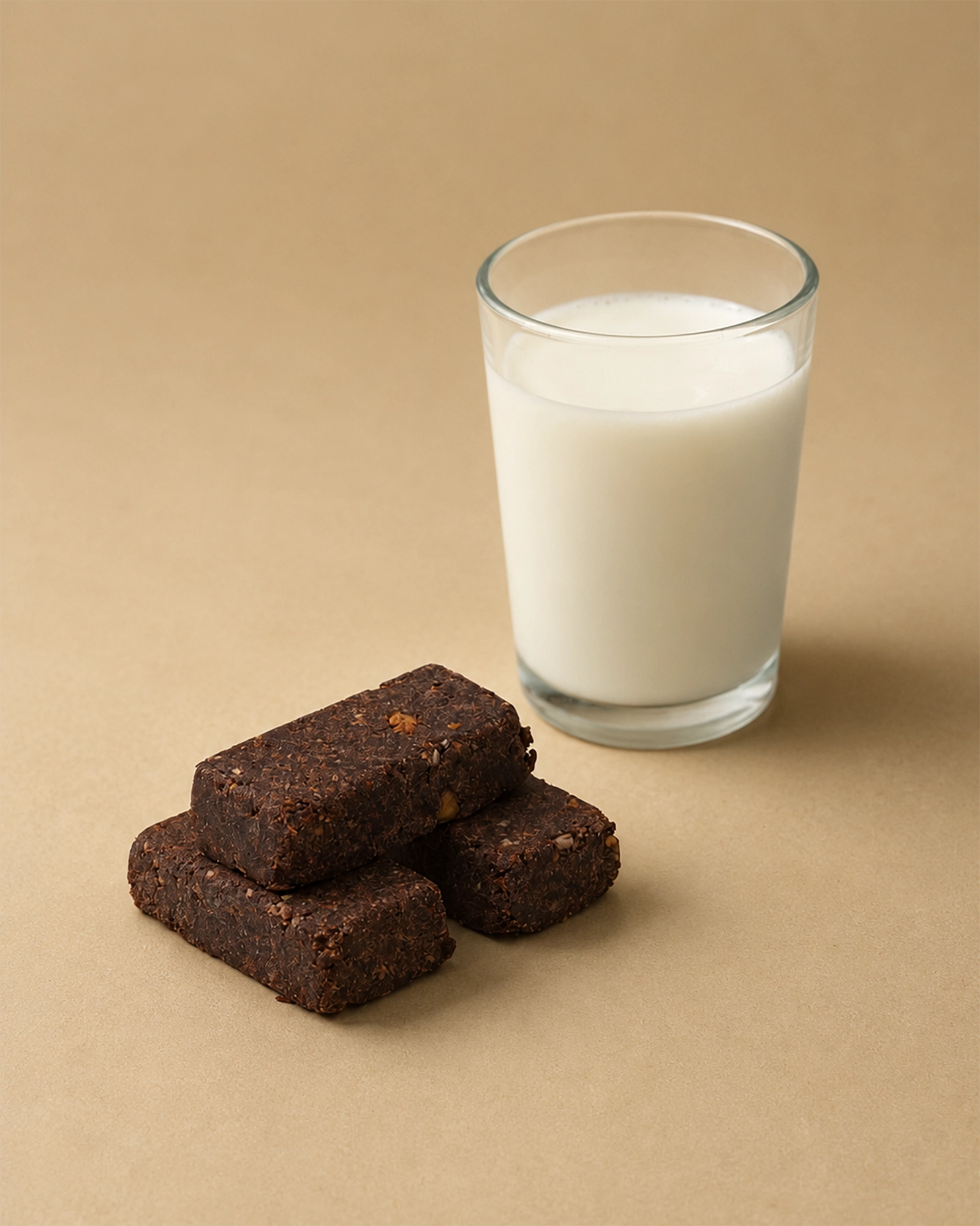 Three Brüt Bar chocolate bites beside a glass of milk on a beige background.