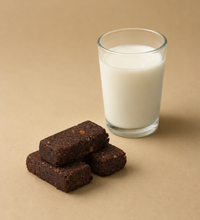 Three Brüt Bar chocolate bites beside a glass of milk on a beige background.