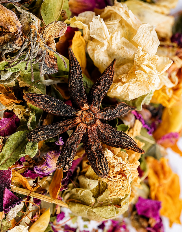 Jar of Signaturi-Tea with dried herbs on a table with a cup of tea and a wooden bowl.