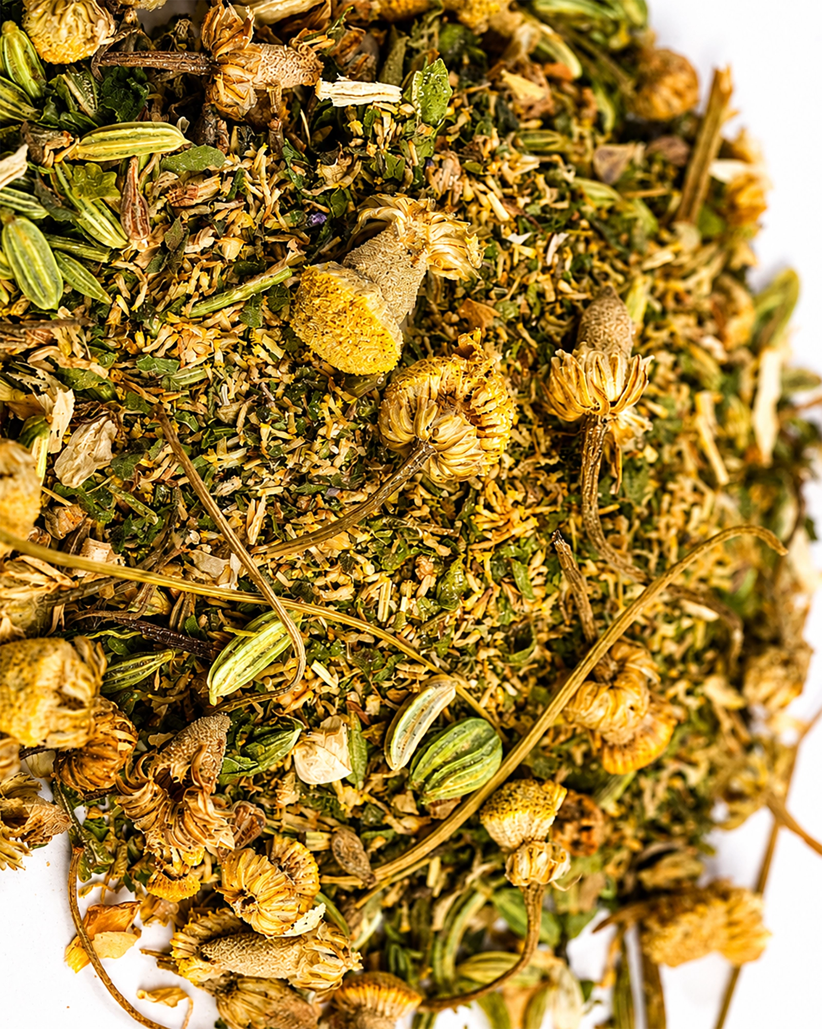 Close-up of De-Bloat Tea herbal blend with dried chamomile flowers and green herbs on a white background.