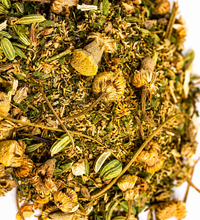 Close-up of De-Bloat Tea herbal blend with dried chamomile flowers and green herbs on a white background.