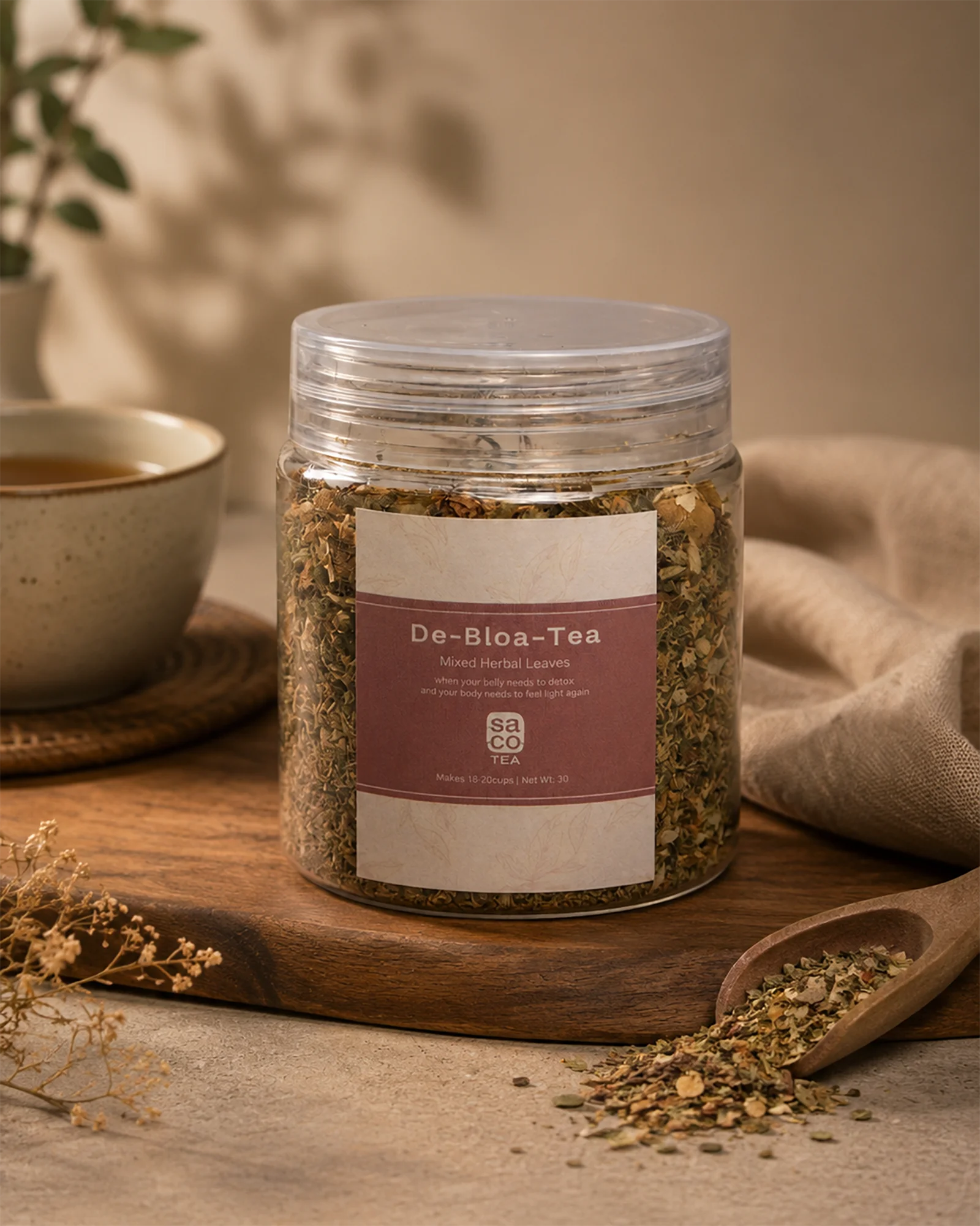 Jar of 'De-Bloa-Tea' with a label on a wooden surface next to a cup and spoon.
