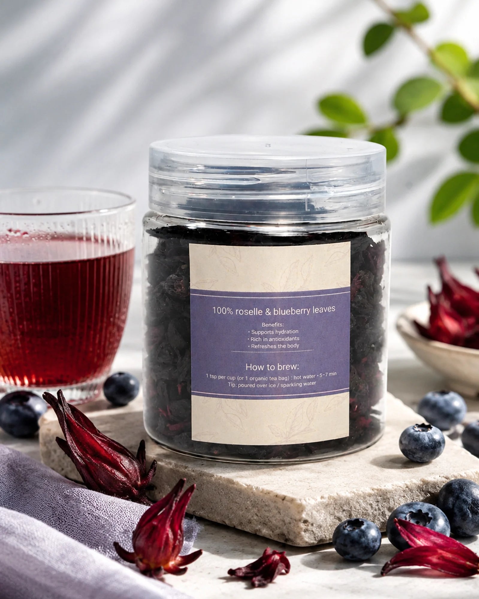Jar of roselle and blueberry leaves with a glass of red juice on a wooden surface.