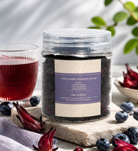 Jar of roselle and blueberry leaves with a glass of red juice on a wooden surface.