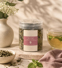 Saco Tea Her Flow herbal tea jar with brewed tea, loose herbs, mint, and soft floral styling on a neutral surface.