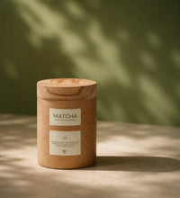 Wooden matcha container with a label on a wooden surface with a green leafy background