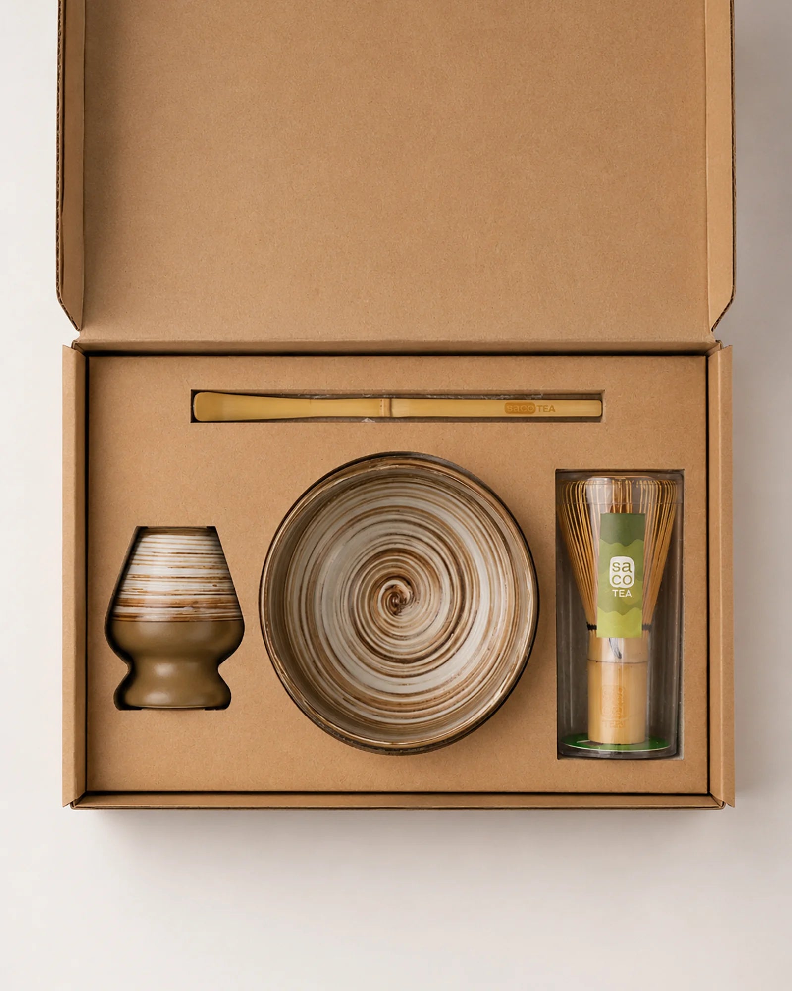 Open Saco Tea earthy matcha gift box with striped ceramic bowl, bamboo whisk, whisk holder, and bamboo scoop.