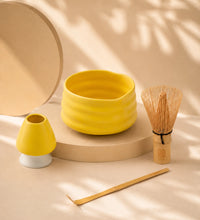 Yellow matcha bowl with bamboo whisk, scoop, and ceramic whisk holder displayed under soft natural shadows.